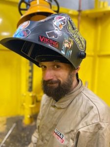 A man wearing welding gear smiles